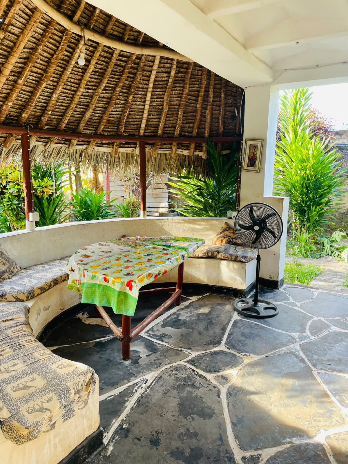 Makuti thatched lounge with built-in bench seating, table and standing fan