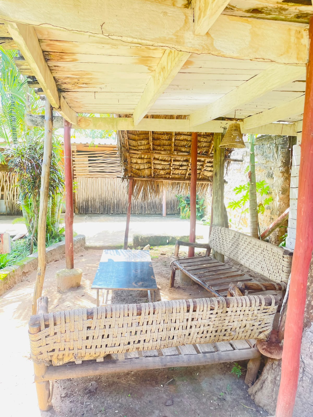 Open shaded lounge with woven rope benches and a low table on the grounds